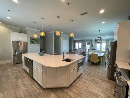 Modern kitchen with an island, stainless steel appliances, pendant lights, and an open dining area. Bright and spacious design.