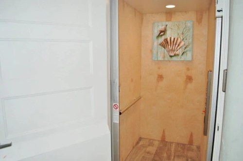 Interior of a small elevator with wooden walls and a seashell artwork on display.