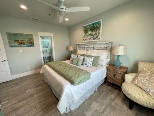 Cozy bedroom with a large bed, decorative pillows, a nightstand, and beach-themed artwork on the walls.