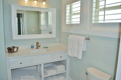 Bright bathroom with a mirror, sink, white towels, and a basket on a countertop, featuring light green walls.