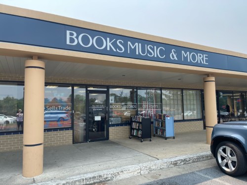 Storefront of "Books Music & More," featuring a sign and a display of books outside.