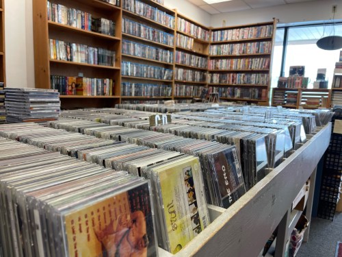 A view of a store interior filled with rows of CDs and DVDs, with shelves lined with more media in the background.