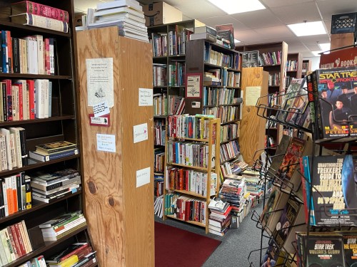 A cozy bookstore aisle filled with shelves of books, wooden dividers, and a display rack of various titles.