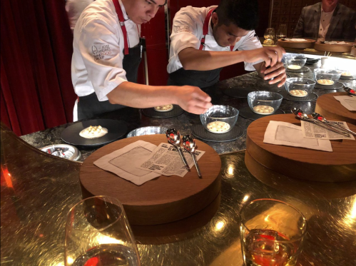 Two chefs in white uniforms prepare dishes at a stylish restaurant, focusing on plating in a luxurious setting.