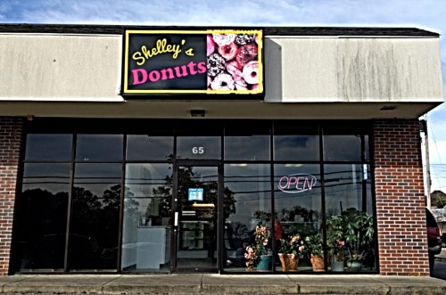 A storefront of "Shelley's Donuts" with a bright sign and an "OPEN" neon light in the window.