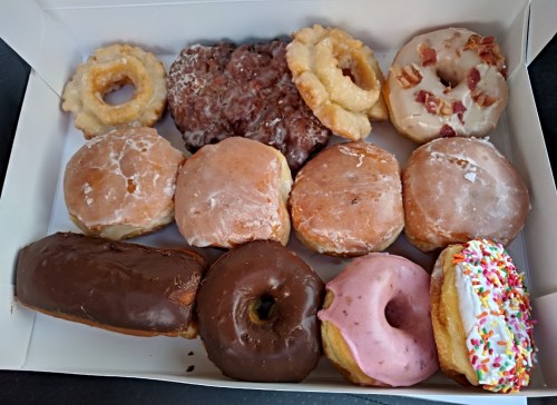 A box of assorted donuts, including glazed, chocolate, and sprinkled varieties, arranged neatly.