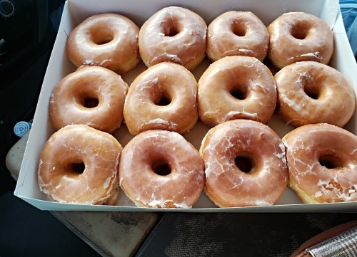A box of twelve glazed donuts, freshly made and arranged neatly.