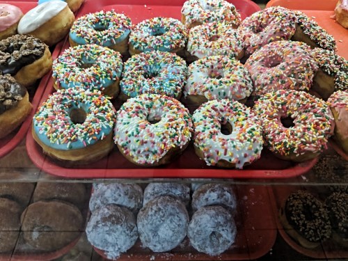 A display of colorful donuts with sprinkles, including glazed and powdered varieties, on a red tray.