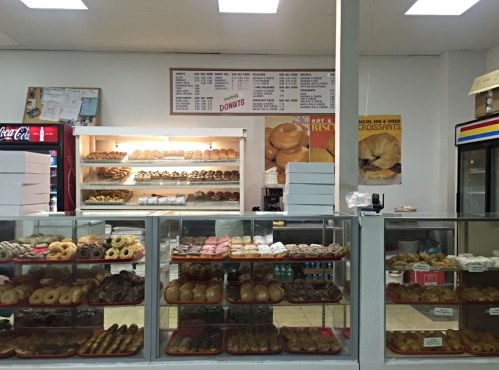 A display case filled with various donuts and pastries in a bakery, with a menu board above.