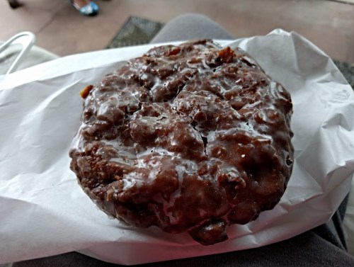 A large, round chocolate-glazed pastry resting on white paper, with a textured surface and a shiny finish.