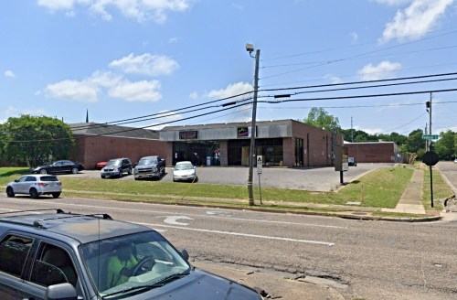 A brick building with storefronts, parked cars, and a clear blue sky in the background.