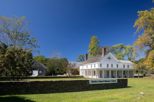 A historic white building with a porch, surrounded by trees and grass, labeled "Shelter Island History Center."