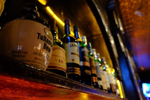 A close-up of a shelf displaying various whiskey bottles in a dimly lit bar.