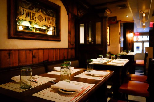 A cozy restaurant interior with wooden walls, tables set with glasses and napkins, and warm lighting.