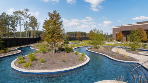 A winding water feature surrounded by greenery and trees under a clear blue sky.