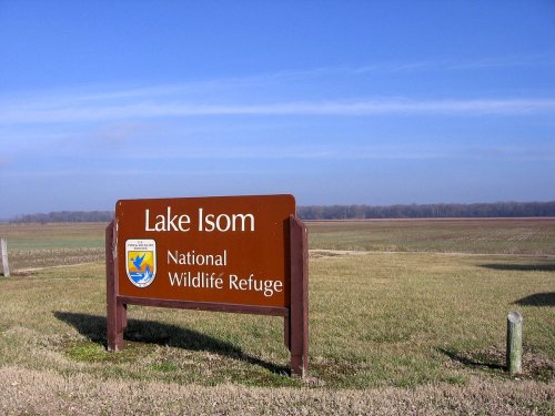 Sign for Lake Isom National Wildlife Refuge, with open fields and a clear blue sky in the background.