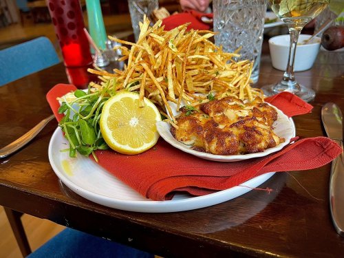 A plate with crispy fries, a lemon wedge, and a serving of baked seafood, garnished with fresh greens on a red napkin.