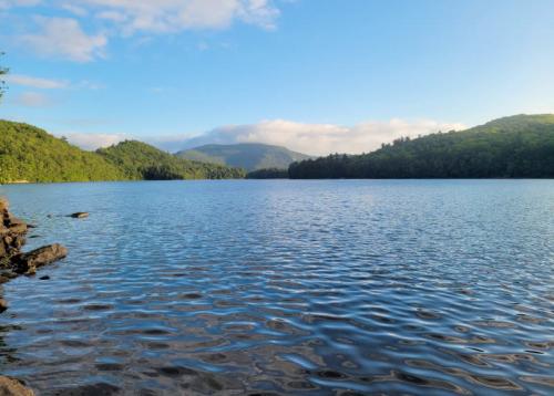 A serene lake surrounded by lush green hills under a clear blue sky with gentle ripples on the water's surface.