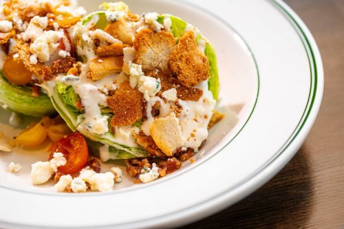 A fresh salad with lettuce, cherry tomatoes, crumbled cheese, and crunchy toppings drizzled with dressing in a bowl.