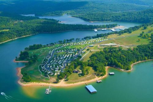 Aerial view of a lush green landscape with a lake, docks, and a campground along the shoreline.