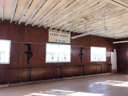 Interior of a roller skating rink with wooden walls, windows, and a sign reading "Roller Skating Every Night 7 to 10."