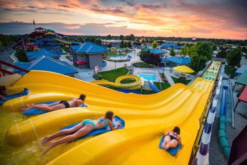 Aerial view of a water park at sunset, featuring yellow water slides and people sliding down into the pool below.