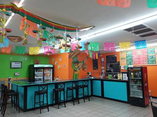 Colorful interior of a Mexican restaurant with festive decorations, a bar area, and a vibrant mural on the wall.