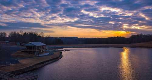 A serene lake at sunset, with a wooden pavilion and clouds reflecting on the water's surface.