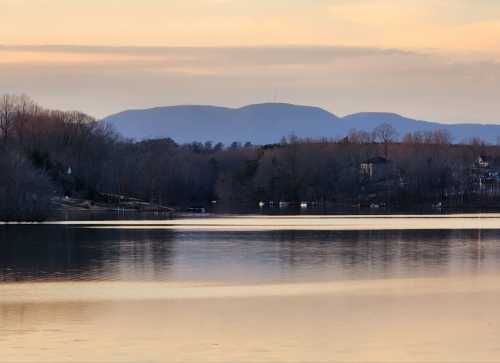 Serene lake view at sunset, with mountains in the background and trees lining the shore.