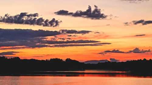 A serene sunset over a calm lake, with vibrant orange and purple hues reflecting on the water and clouds in the sky.