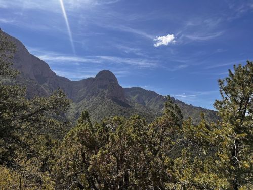 A scenic view of mountains and lush greenery under a bright blue sky with wispy clouds.