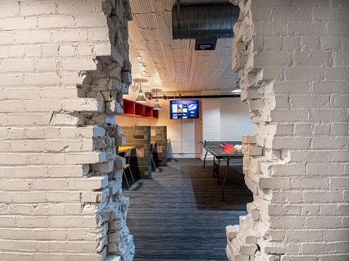 A view through a partially demolished wall into a modern office space with a TV and colorful furniture.