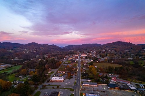 Aerial view of a small town at sunset, surrounded by hills and colorful clouds in the sky.