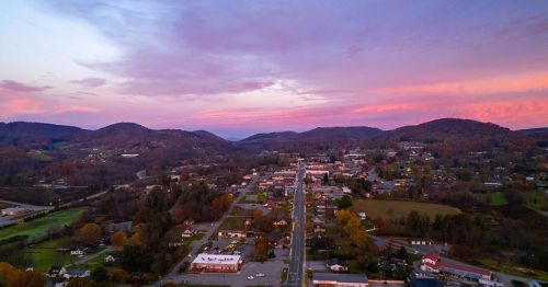 Aerial view of a small town surrounded by hills at sunset, with colorful skies and a winding road through the landscape.