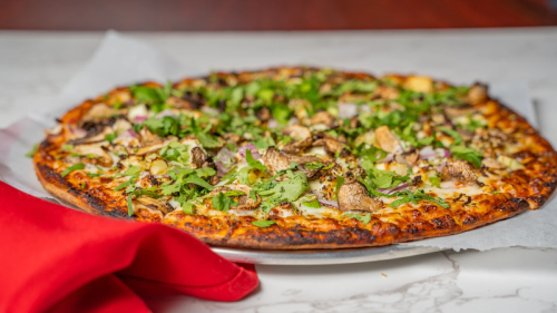 A freshly baked pizza topped with mushrooms, herbs, and cheese, served on a marble table with a red napkin.
