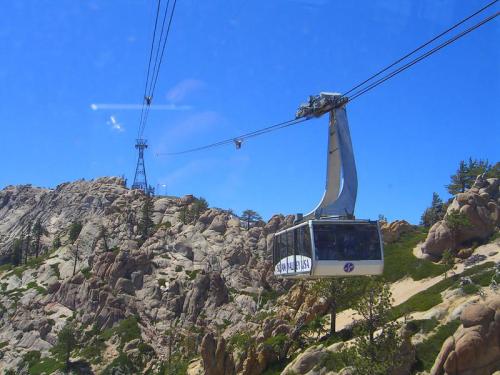 A gondola lifts over rocky terrain under a clear blue sky, connecting two mountain points.