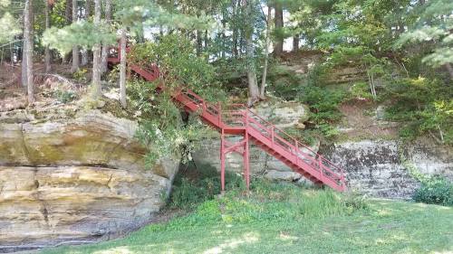 A red staircase leads up a rocky hillside, surrounded by trees and greenery.
