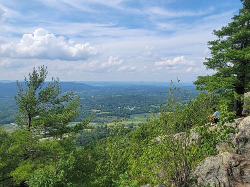 A scenic view from a rocky overlook, featuring lush greenery and rolling hills under a partly cloudy sky.
