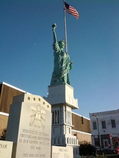 Statue of Liberty replica with an American flag, next to a memorial honoring veterans of five wars.