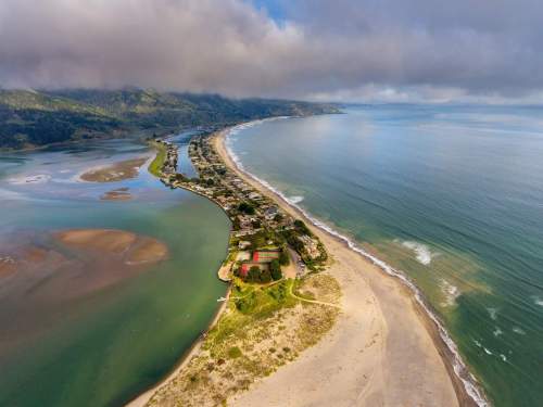 Aerial view of a coastal landscape featuring a sandy beach, calm waters, and a small town along the shoreline.