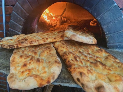 Freshly baked flatbreads cooling in a traditional oven with flames in the background.
