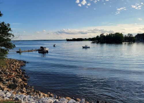 A serene lake scene with boats on the water, a dock, and rocky shoreline under a clear blue sky.