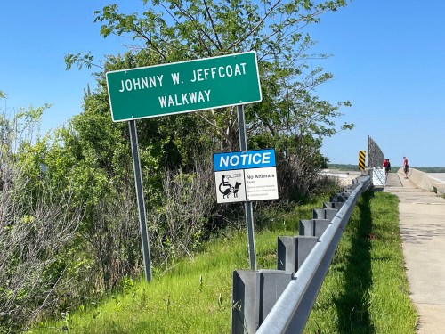 Sign for Johnny W. Jeffcoat Walkway with a notice about no animals, alongside a paved path and greenery.