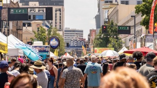 A bustling street fair in Reno, with colorful tents, crowds of people, and bright signage under a clear blue sky.