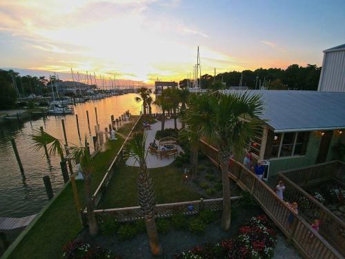 A scenic waterfront view at sunset, featuring palm trees, a marina, and a cozy outdoor seating area.
