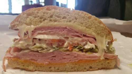 A cross-section of a sandwich with layers of ham, turkey, lettuce, tomato, and mayonnaise on a soft bread roll.