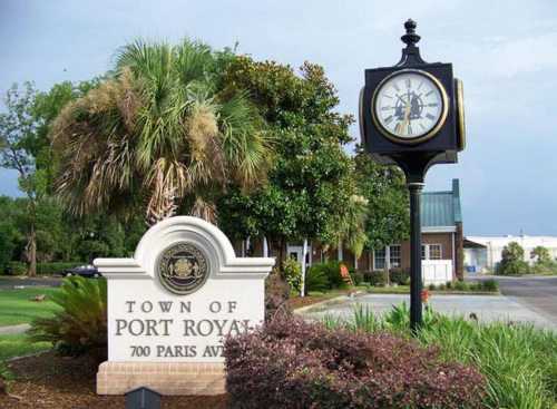 Sign for the Town of Port Royal with a clock nearby, surrounded by greenery and a cloudy sky.