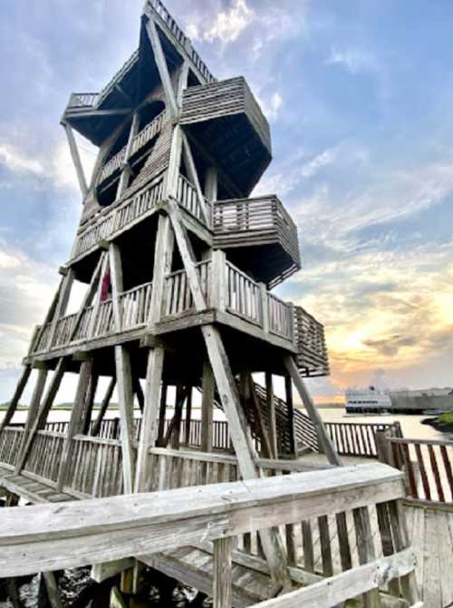 A tall wooden observation tower with multiple levels, set against a colorful sunset over a body of water.