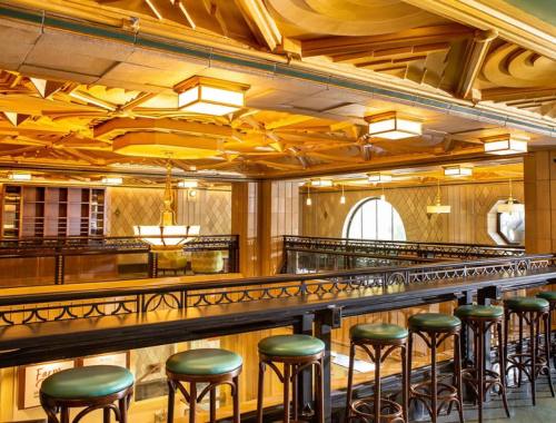 Elegant interior of a restaurant with ornate wooden ceilings and bar seating, featuring large windows and warm lighting.