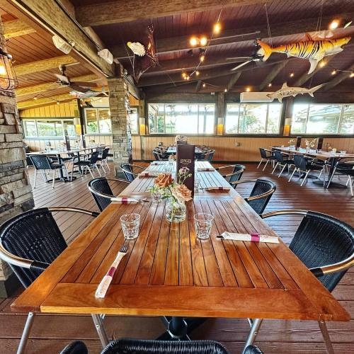A wooden dining table set for a meal in a rustic restaurant with large windows and decorative fish overhead.